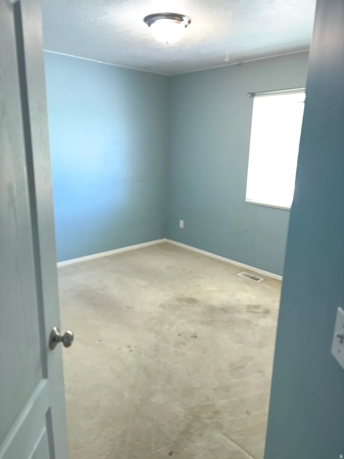 Room featuring wall-to-wall carpeting, light blue wall paint, a single window with blinds, and an overhead flush-mount light fixture