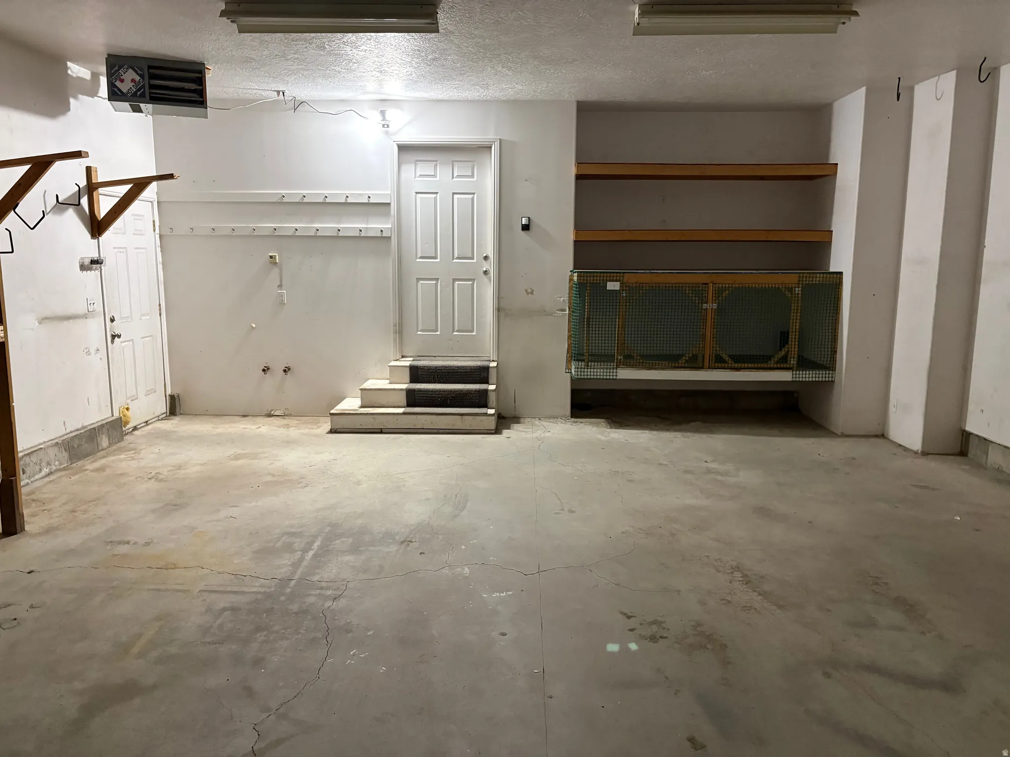 Spacious garage featuring a concrete floor, built-in shelving, an interior access door with steps, and overhead lighting