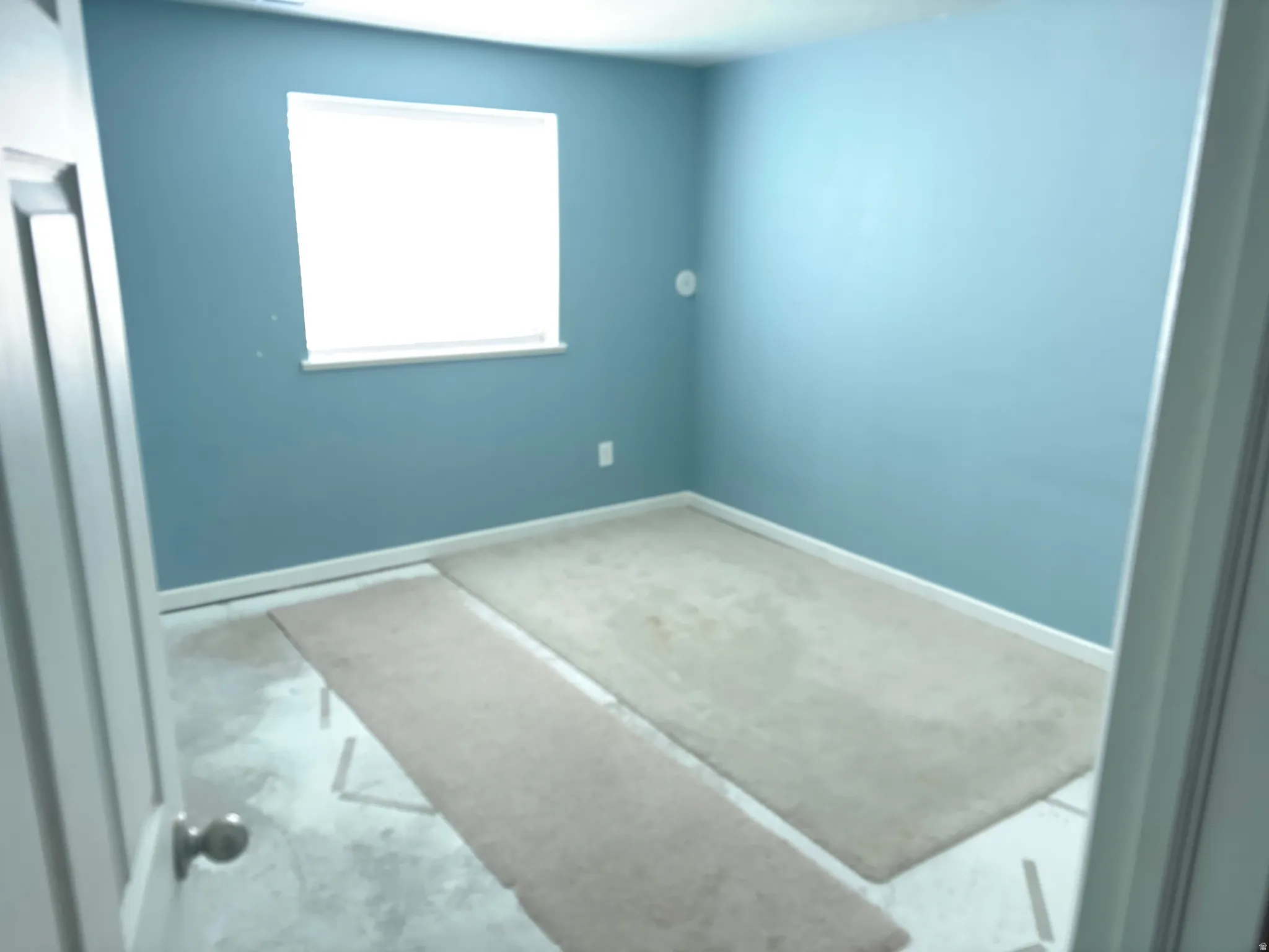 Room with blue walls and a single window, featuring white trim and baseboards