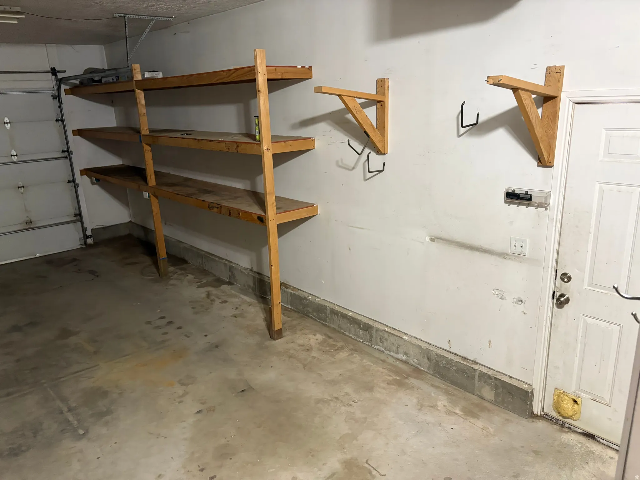 Garage area featuring built-in wooden shelving units, additional wall-mounted storage brackets, a concrete floor, and a white access door