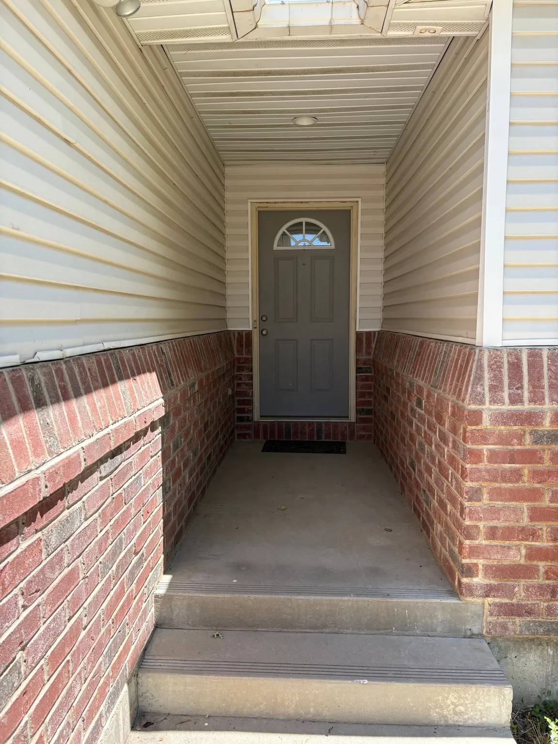 Recessed entryway featuring a gray panel door with an arched glass insert, flanked by brick masonry and beige siding