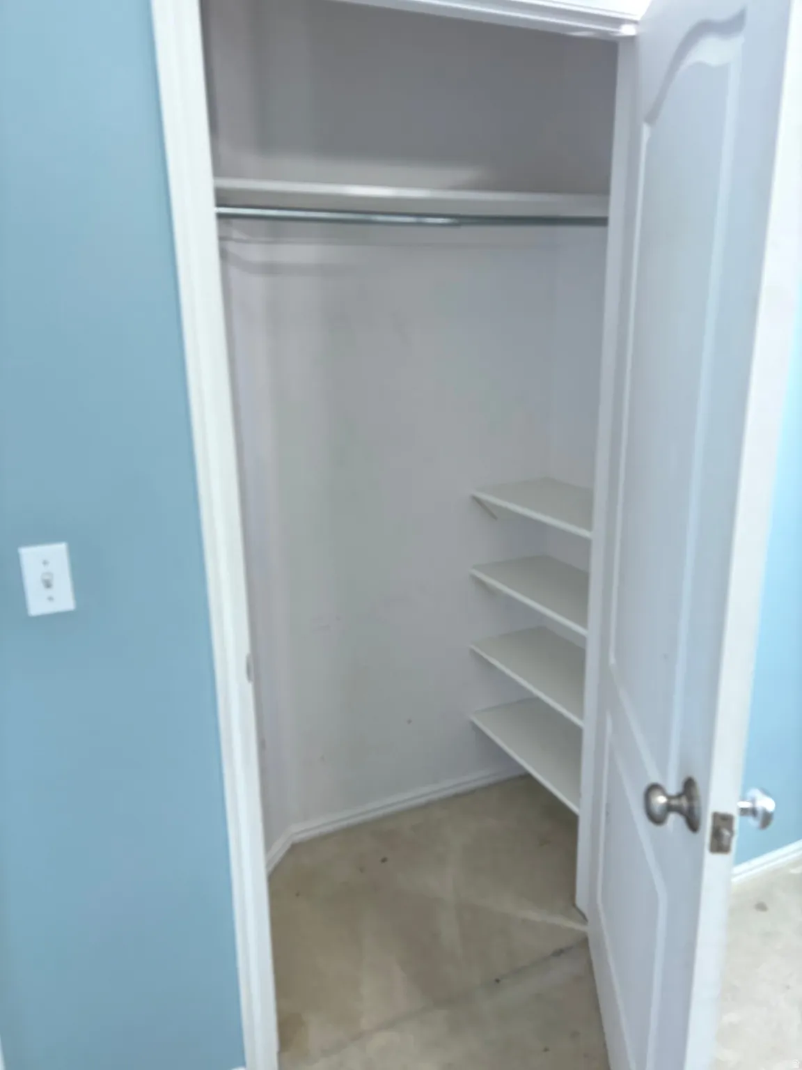Bedroom Recessed closet featuring a metal hanging rod, three built-in shelves, and a paneled door with a silver-tone knob