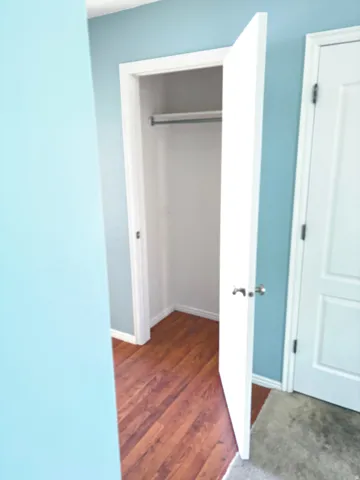 Open closet featuring a metal hanging rod and wood-finish flooring
