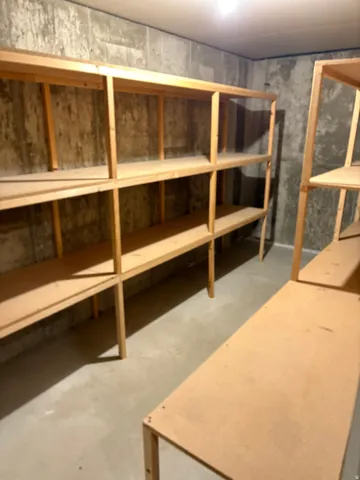 Utility area featuring extensive built-in wooden shelving units, concrete walls, concrete flooring, and overhead lighting