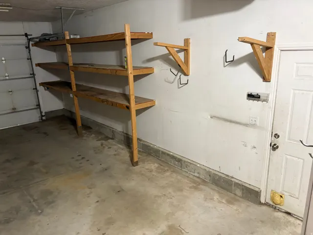 Garage area featuring built-in wooden shelving units, additional wall-mounted storage brackets, a concrete floor, and a white access door