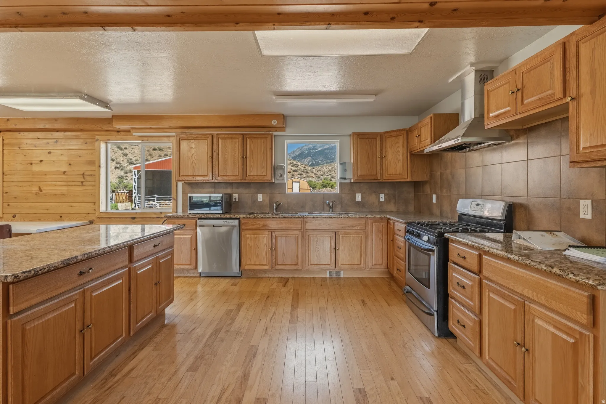 Spacious kitchen featuring wood-finish flooring, light wood cabinetry, stone countertops, and stainless steel appliances