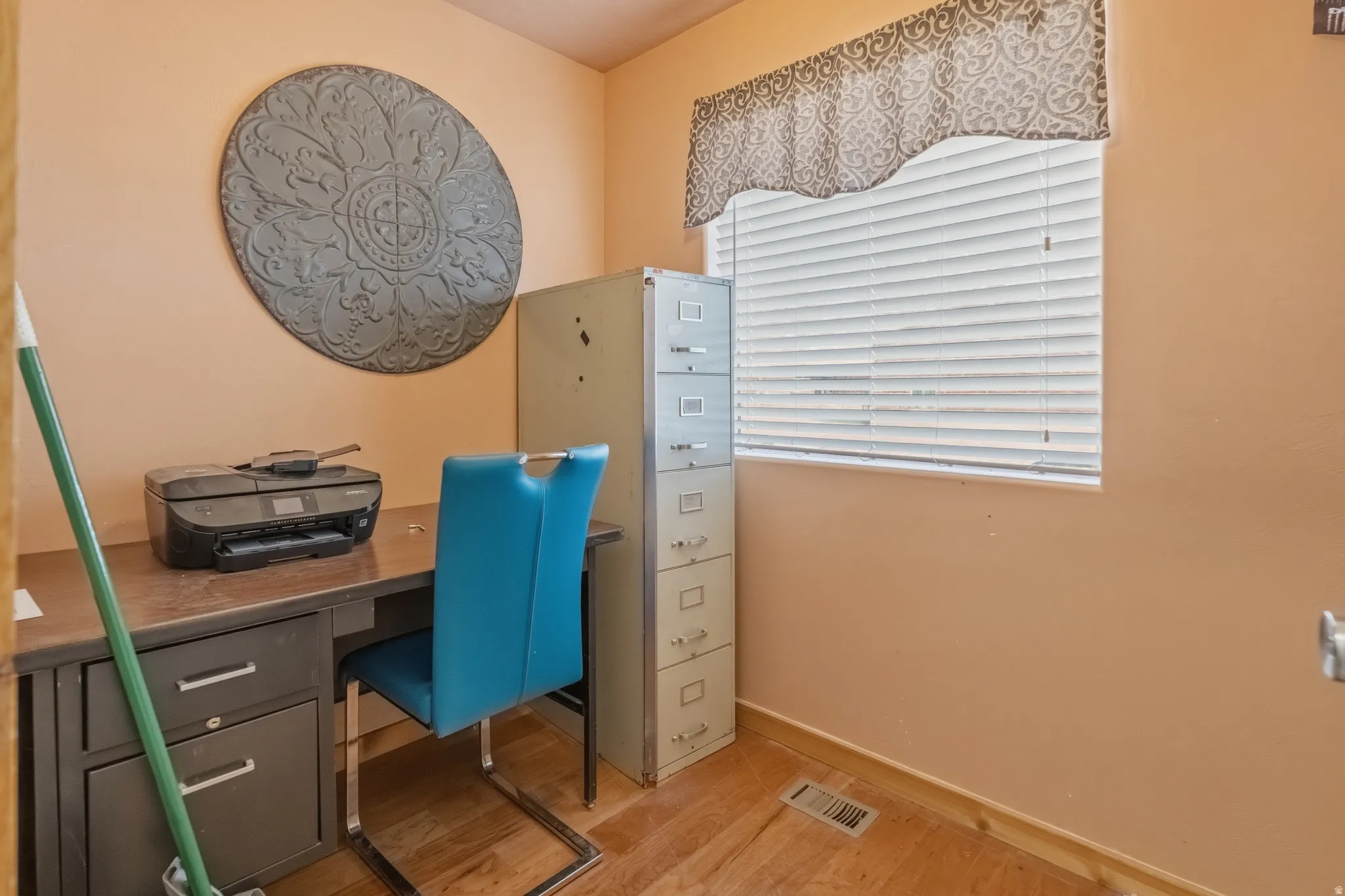 Dedicated office space with a built-in desk featuring dark wood-finish cabinetry, a window with horizontal blinds, and warm-toned wall paint