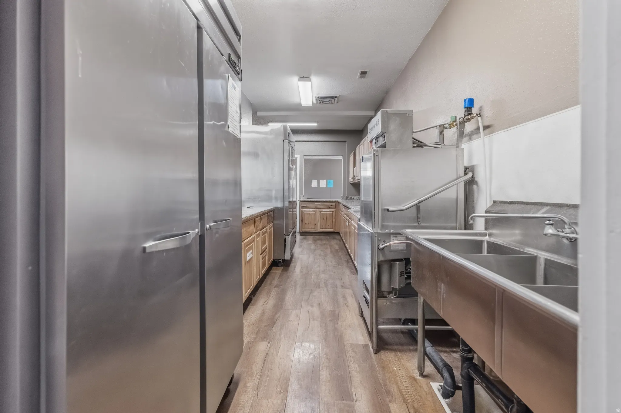 Commercial kitchen featuring stainless steel appliances, wood-finish flooring, and a multi-basin sink