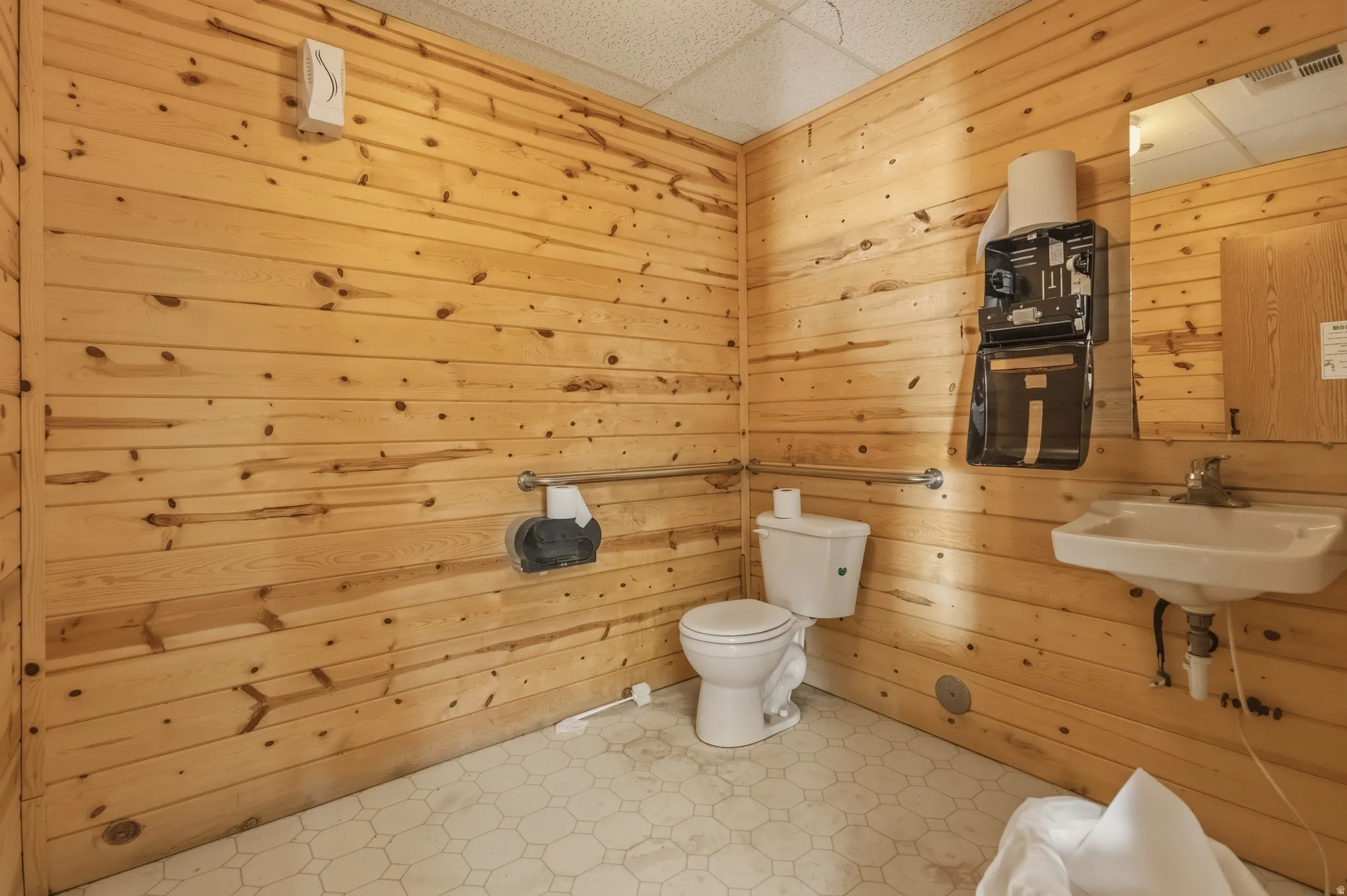 Restroom featuring wood-paneled walls, a white pedestal sink, a toilet, and a large mirror