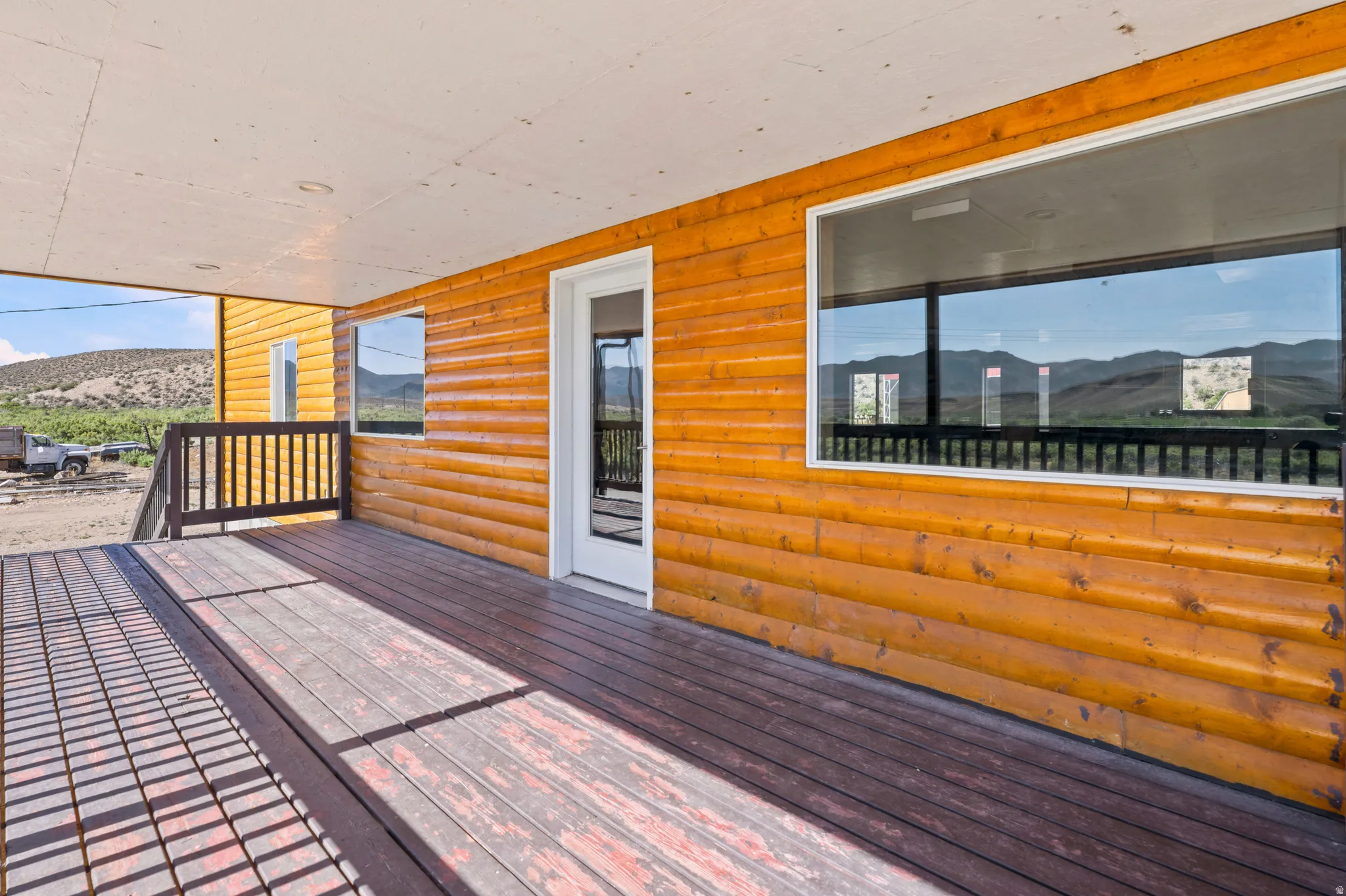 Covered porch featuring wood plank decking, a white exterior door with glass insert, horizontal wood panel siding, and two large windows