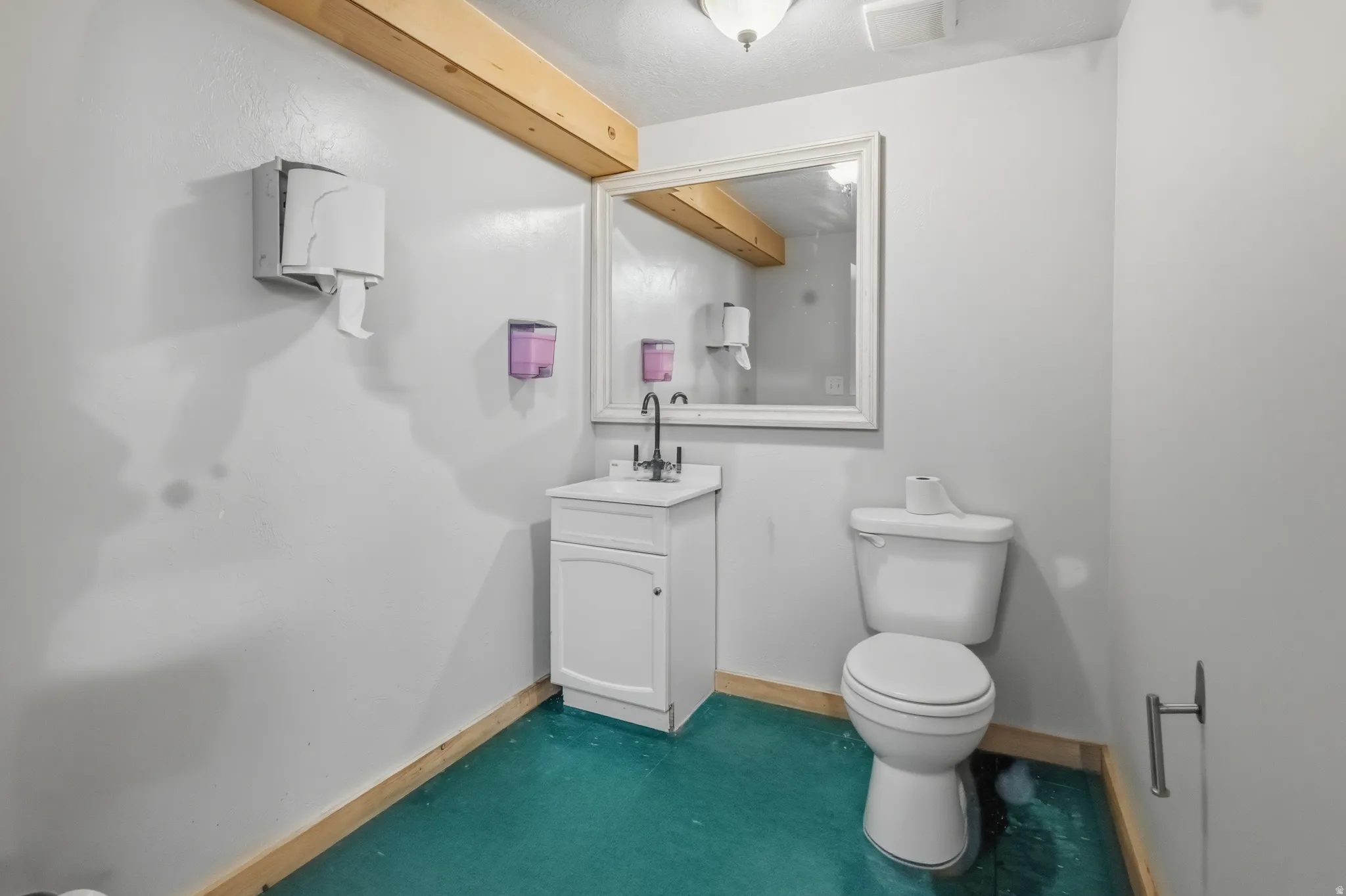 Restroom featuring a white vanity with a black faucet, a framed mirror, a toilet, and teal flooring