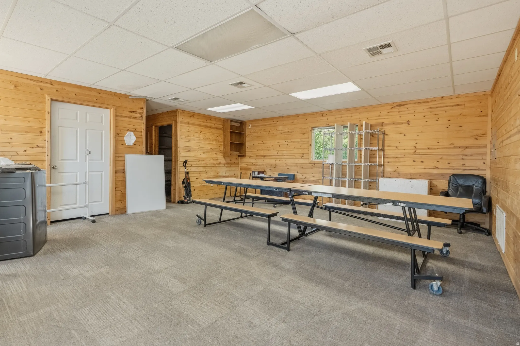 Spacious room featuring wood-finish wall paneling, a neutral-toned carpet, and a drop ceiling with integrated lighting