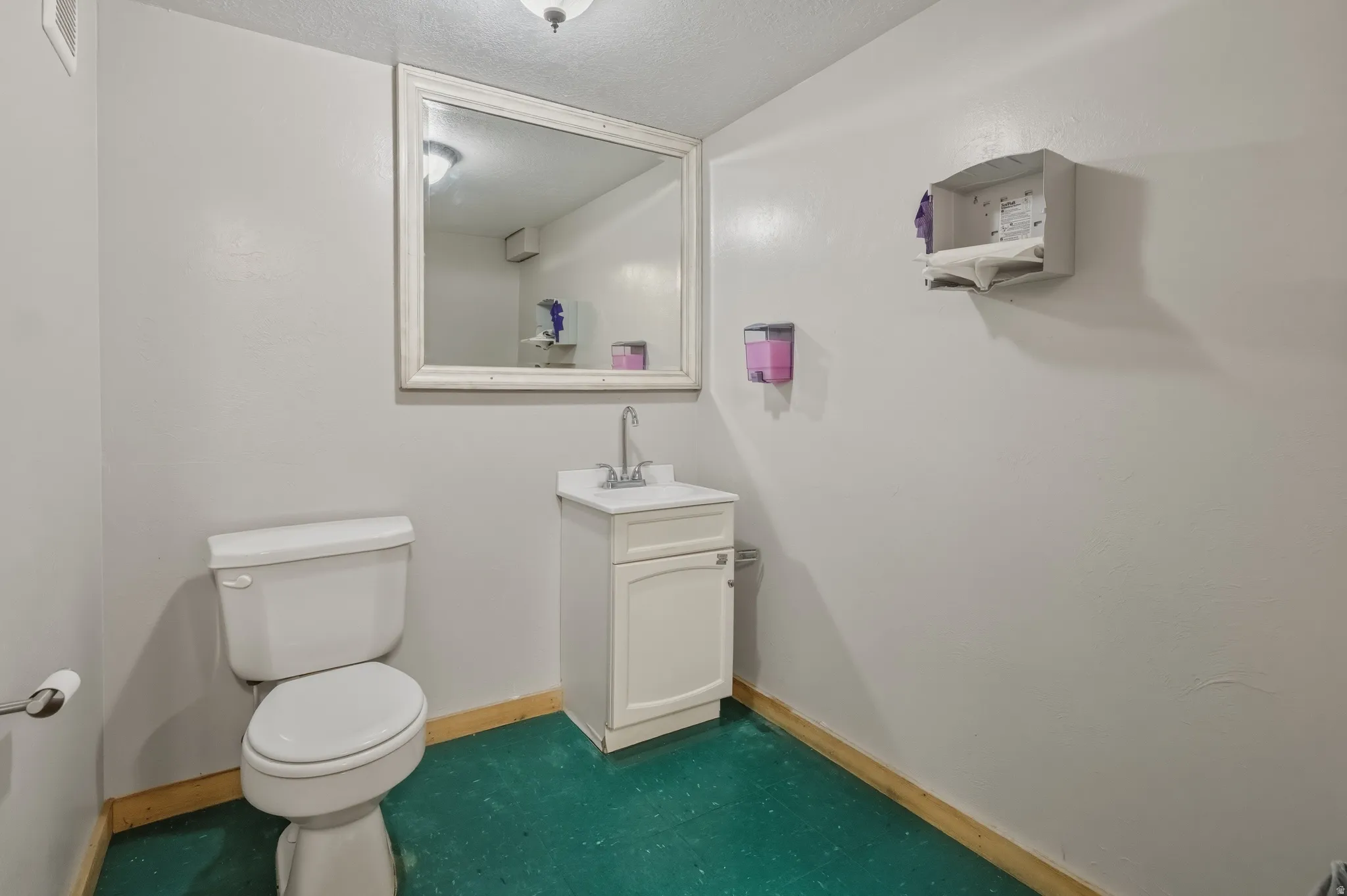 Restroom featuring a white toilet, freestanding vanity with a single sink and chrome faucet, and a wall-mounted mirror with a distressed frame