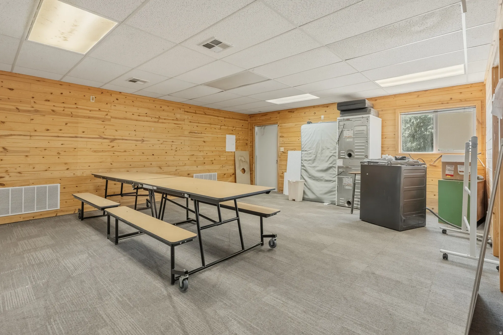 Spacious room featuring wood-paneled walls, a drop ceiling with recessed lighting, and grey patterned flooring