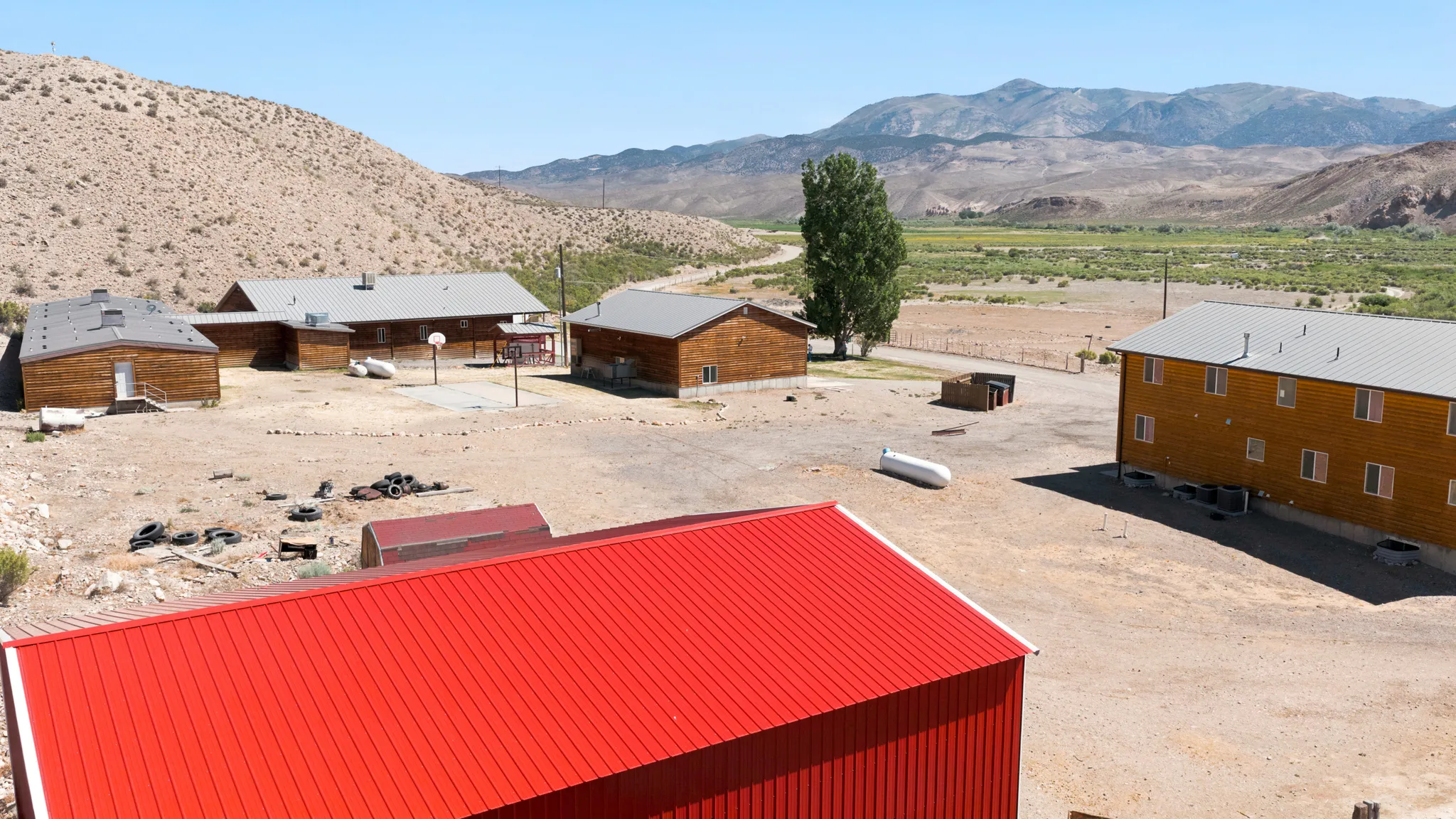 Multiple residential structures featuring wood siding and metal roofs, set against a backdrop of arid hills and distant mountains