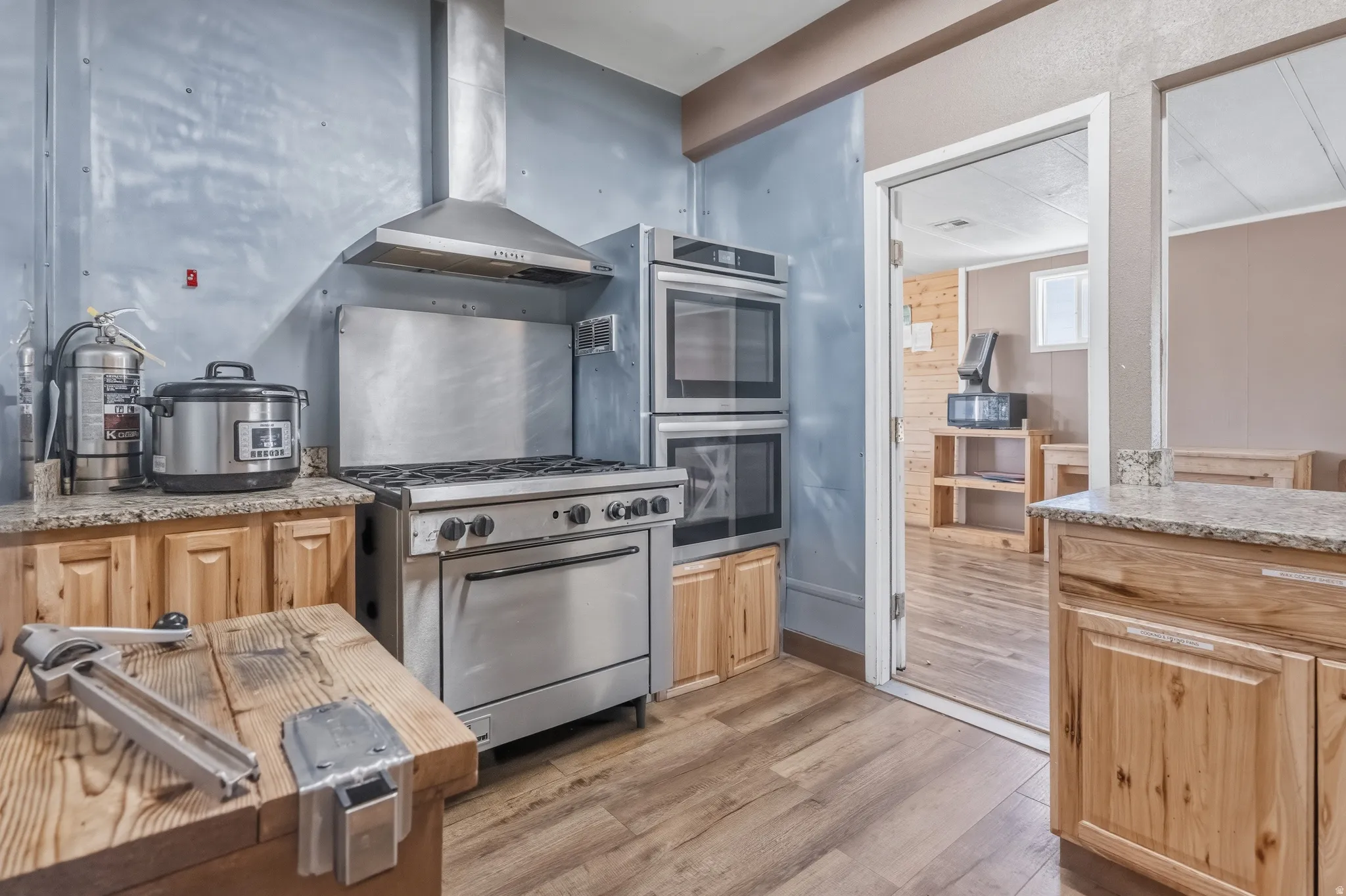 Stainless steel range with a ventilation hood, double wall ovens, granite-finish countertops, and wood-finish cabinetry