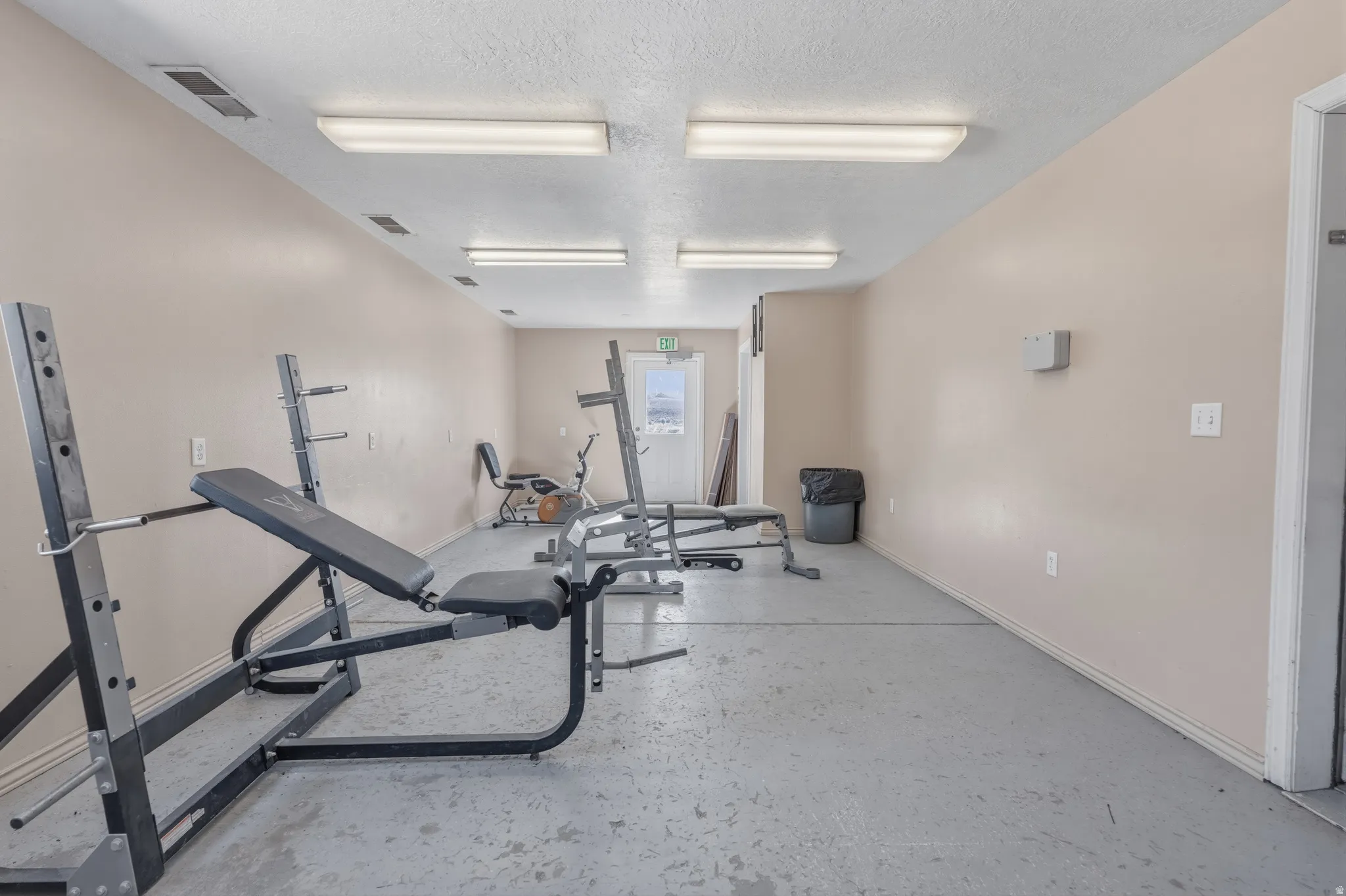 Dedicated fitness area featuring concrete flooring, neutral wall paint, and multiple fluorescent ceiling light fixtures