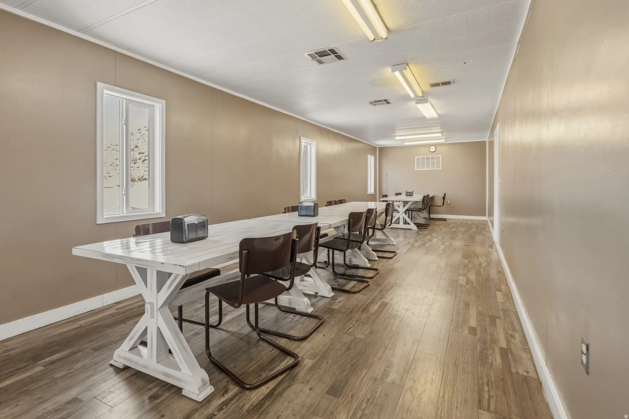 Spacious room featuring wood-finish flooring, neutral-toned walls, multiple rectangular windows, and fluorescent lighting fixtures