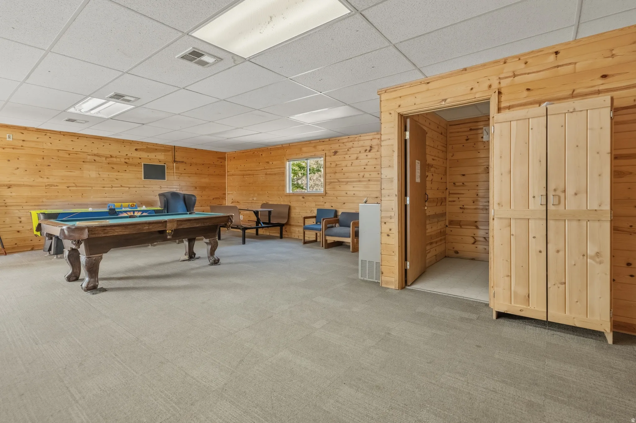 Recreational space featuring extensive wood paneling, recessed lighting, drop ceiling, and light gray carpeting