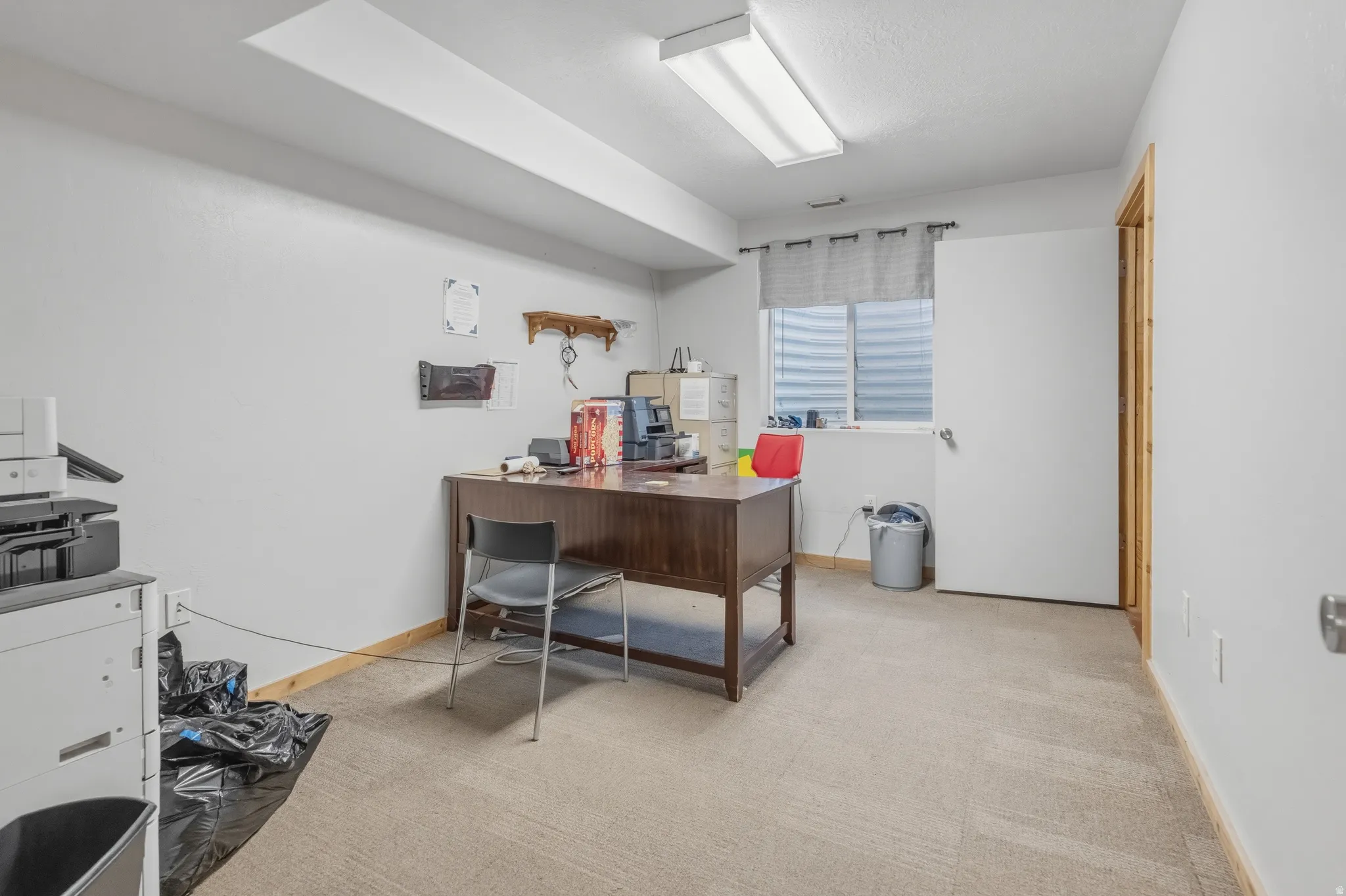 Versatile room featuring light neutral walls, carpeted flooring, a window with horizontal blinds, and a wood-finish door frame