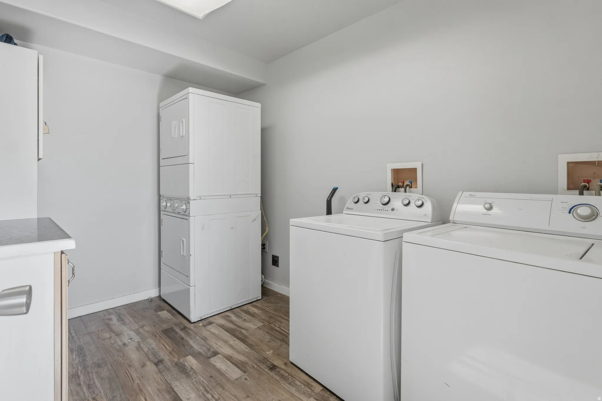 Dedicated laundry area featuring wood-finish flooring, a stacked washer/dryer unit, and a separate side-by-side washer and dryer setup