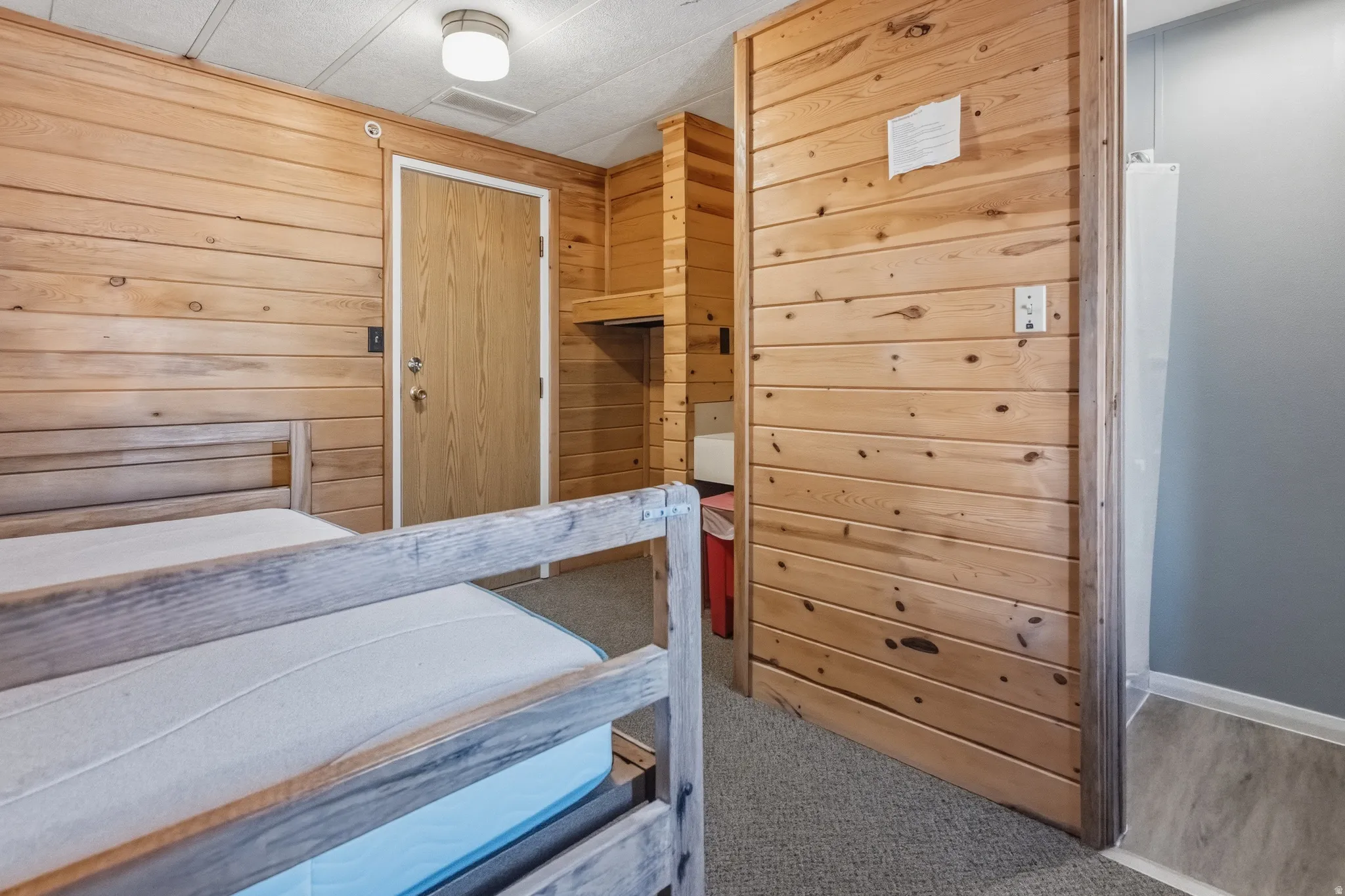 Room featuring extensive wood paneling, a neutral carpeted floor, and a flush-mount ceiling light fixture