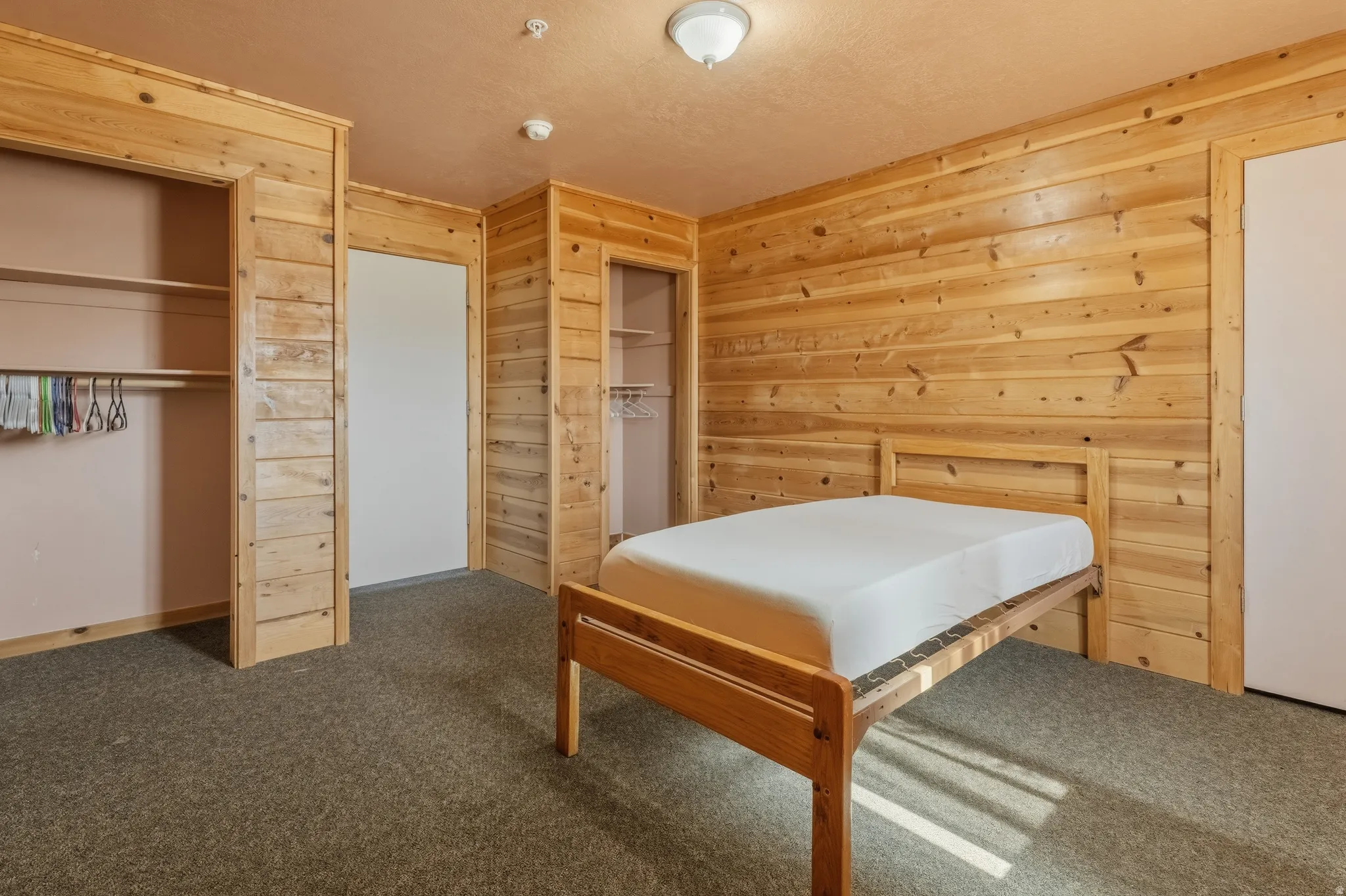 Bedroom featuring wood paneling throughout, dual open closets with shelving and hanging rods, neutral carpet flooring, and a ceiling-mounted light fixture