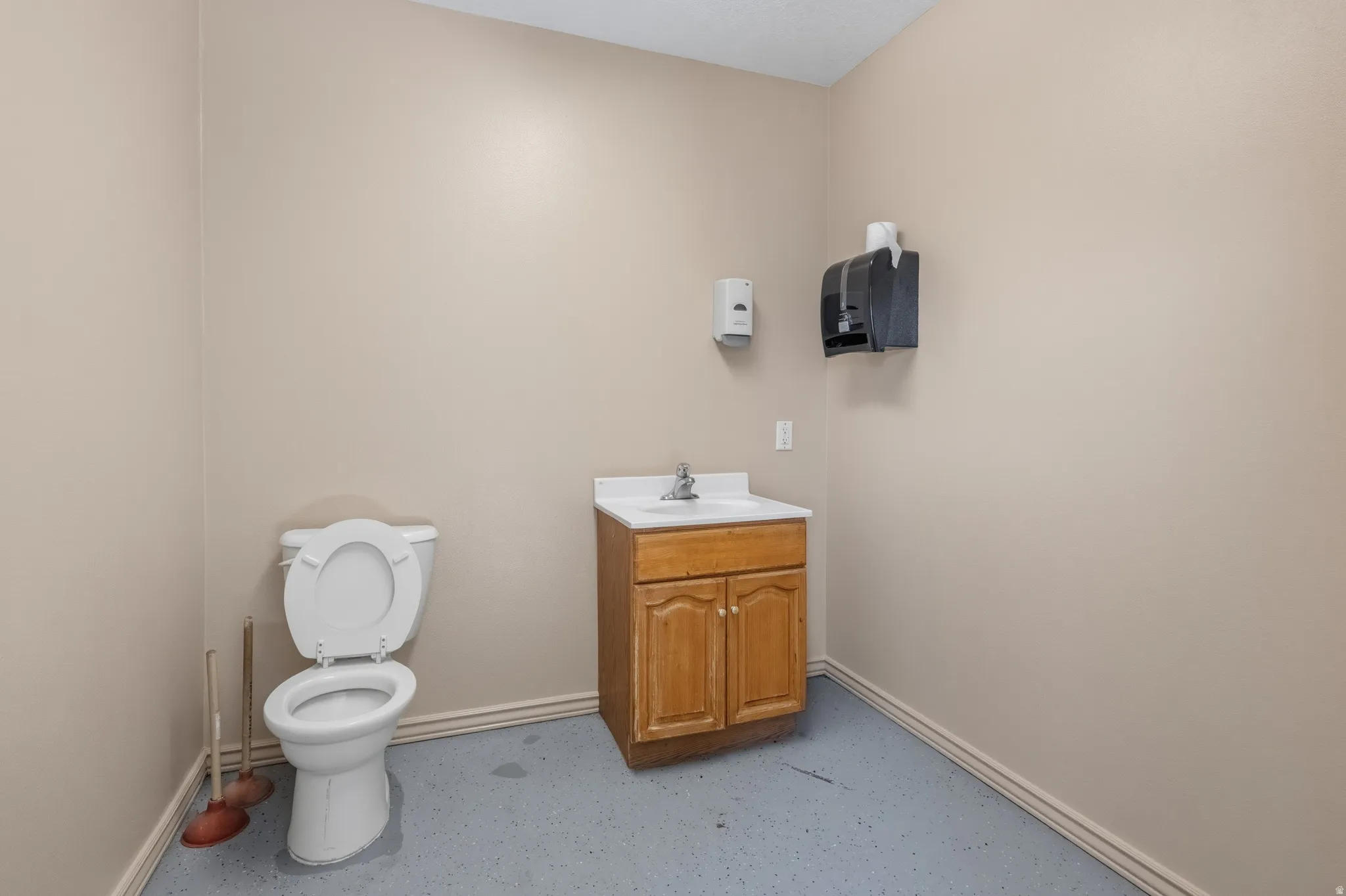 Powder room featuring a white toilet, wood-finish vanity with a white countertop and integrated sink, and gray flooring