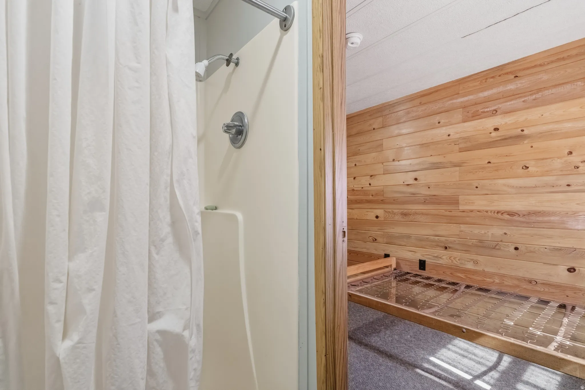 Shower featuring a chrome shower head and controls, a beige surround, and a white shower curtain