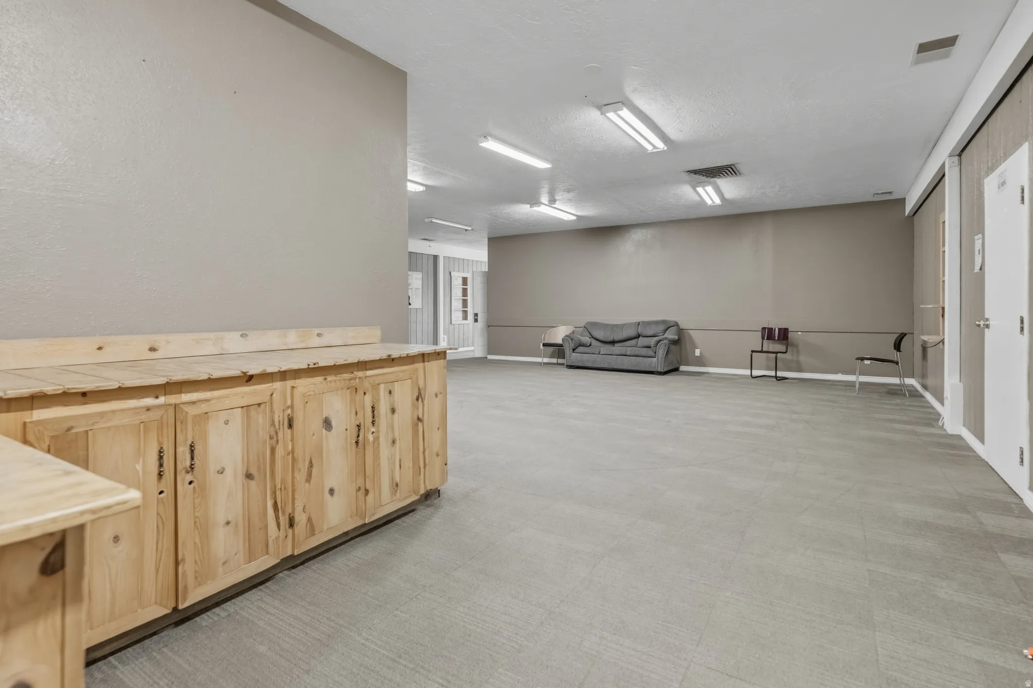 Expansive room featuring light wood cabinetry with surface counter, neutral-toned walls, and grey tile flooring