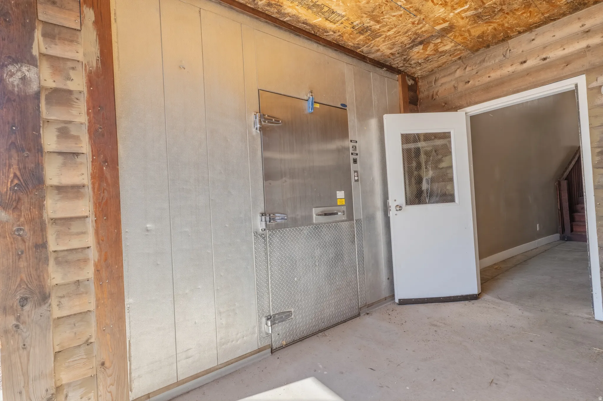 Stainless steel walk-in cooler, wood-paneled walls, and a concrete floor