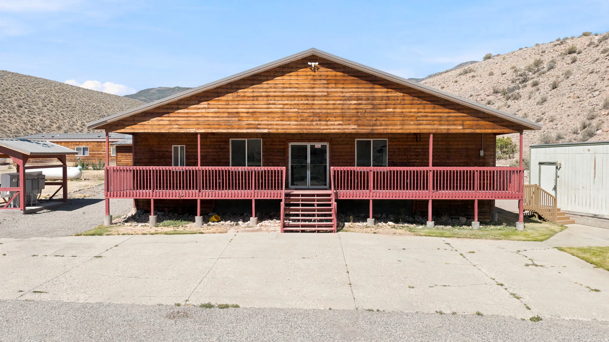 Wood-sided exterior featuring a red-painted elevated deck with stairs and railing, multiple windows, and a central glass-paneled door