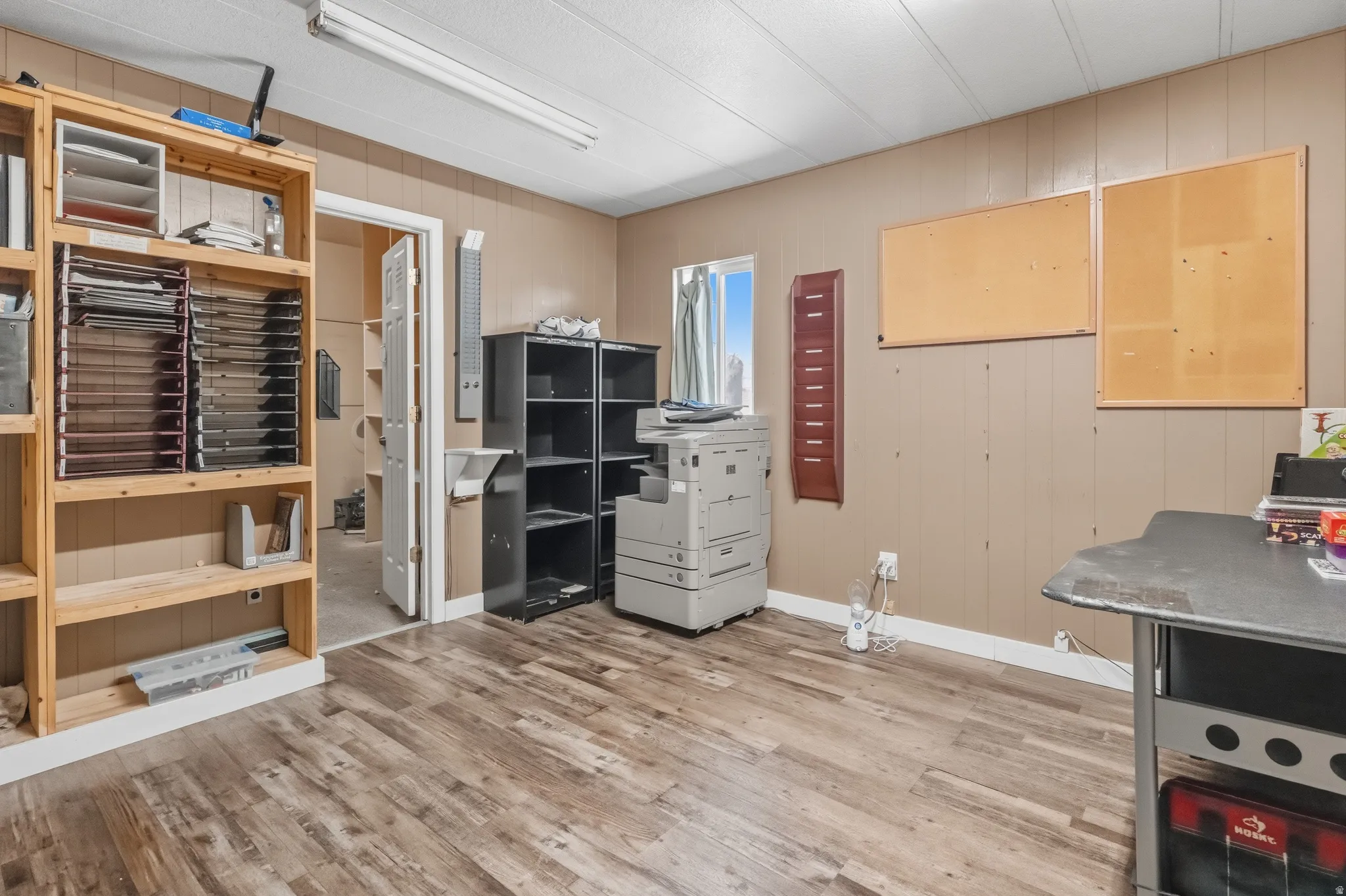 Room featuring wood-finish flooring, built-in wooden shelving, a window with natural light, and paneled walls