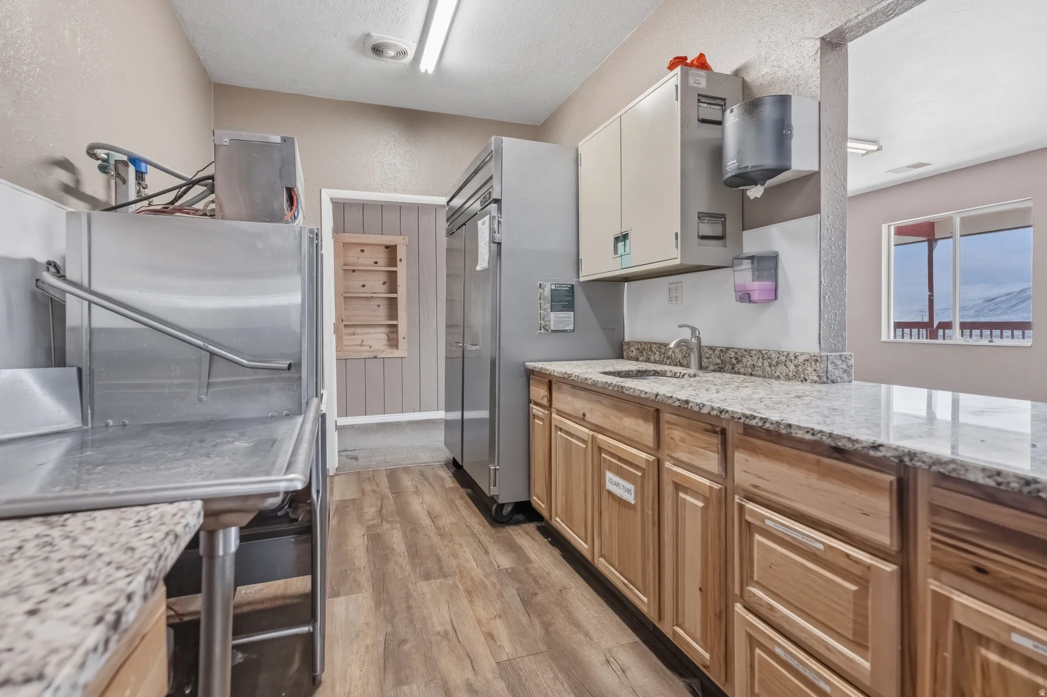 Stainless steel commercial-grade sink and appliances complemented by granite countertops, light wood-finish cabinetry, and wood-finish flooring