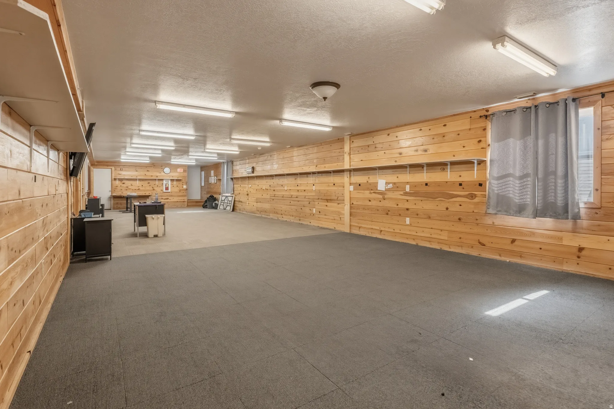 Expansive room featuring wood-paneled walls, a combination of dark and light gray flooring, and multiple fluorescent ceiling lights