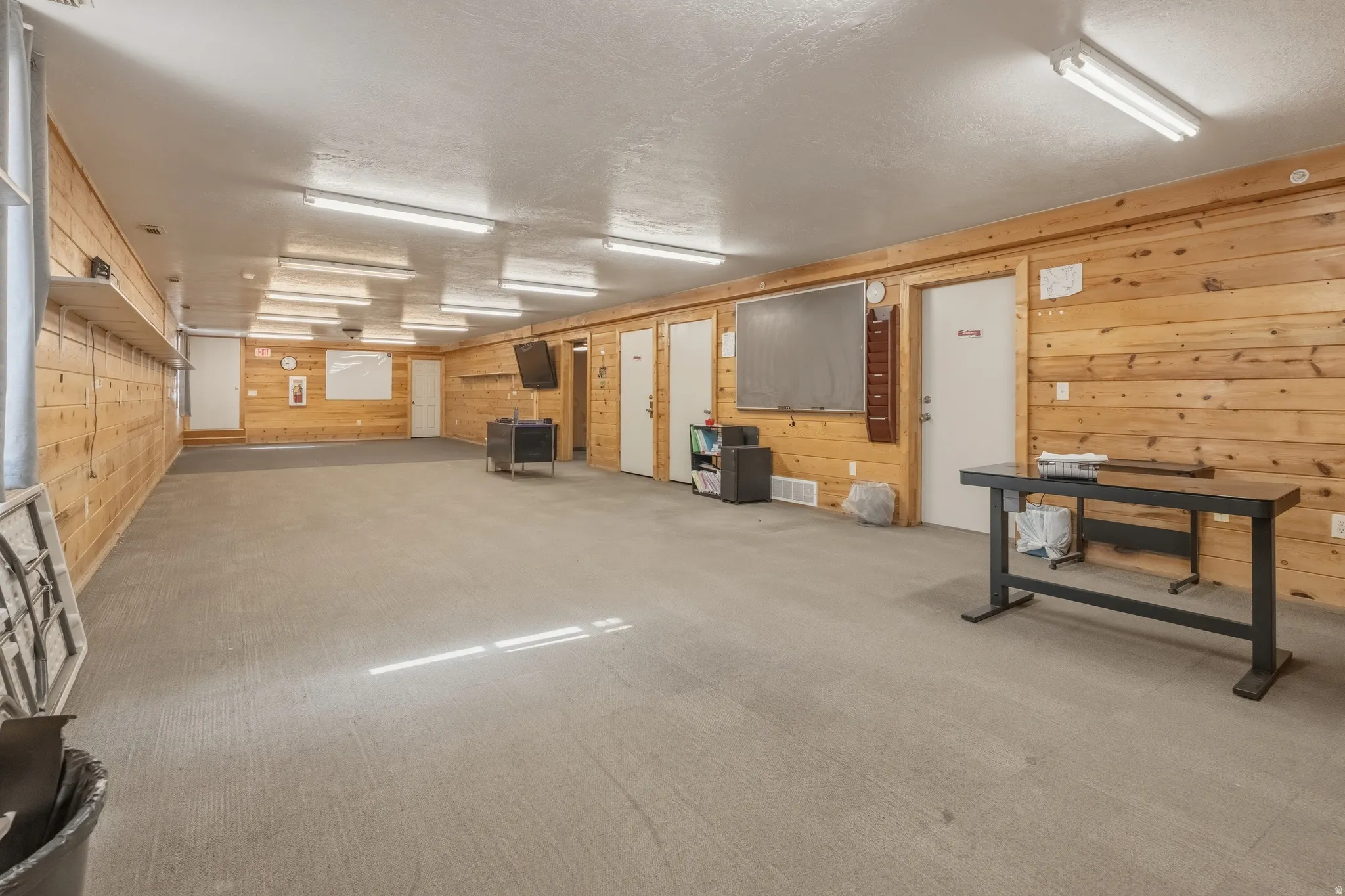 Spacious room featuring wood-paneled walls, a neutral-toned floor, and multiple recessed linear light fixtures