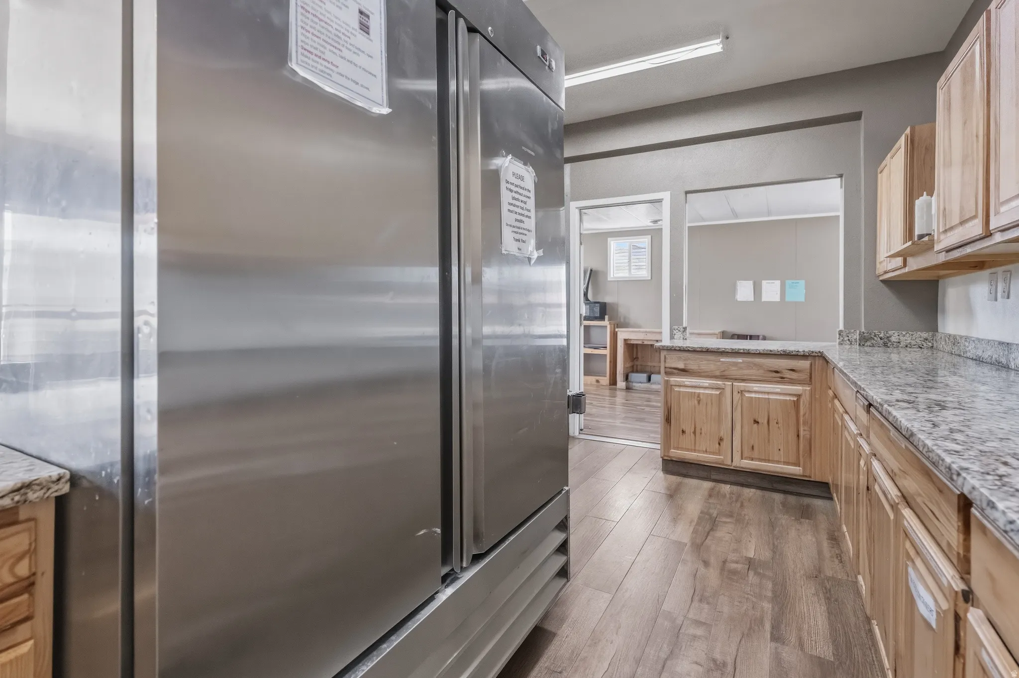 Kitchen area featuring a stainless steel commercial-grade refrigerator, wood-finish flooring, granite countertops, and light wood cabinetry with brushed nickel hardware