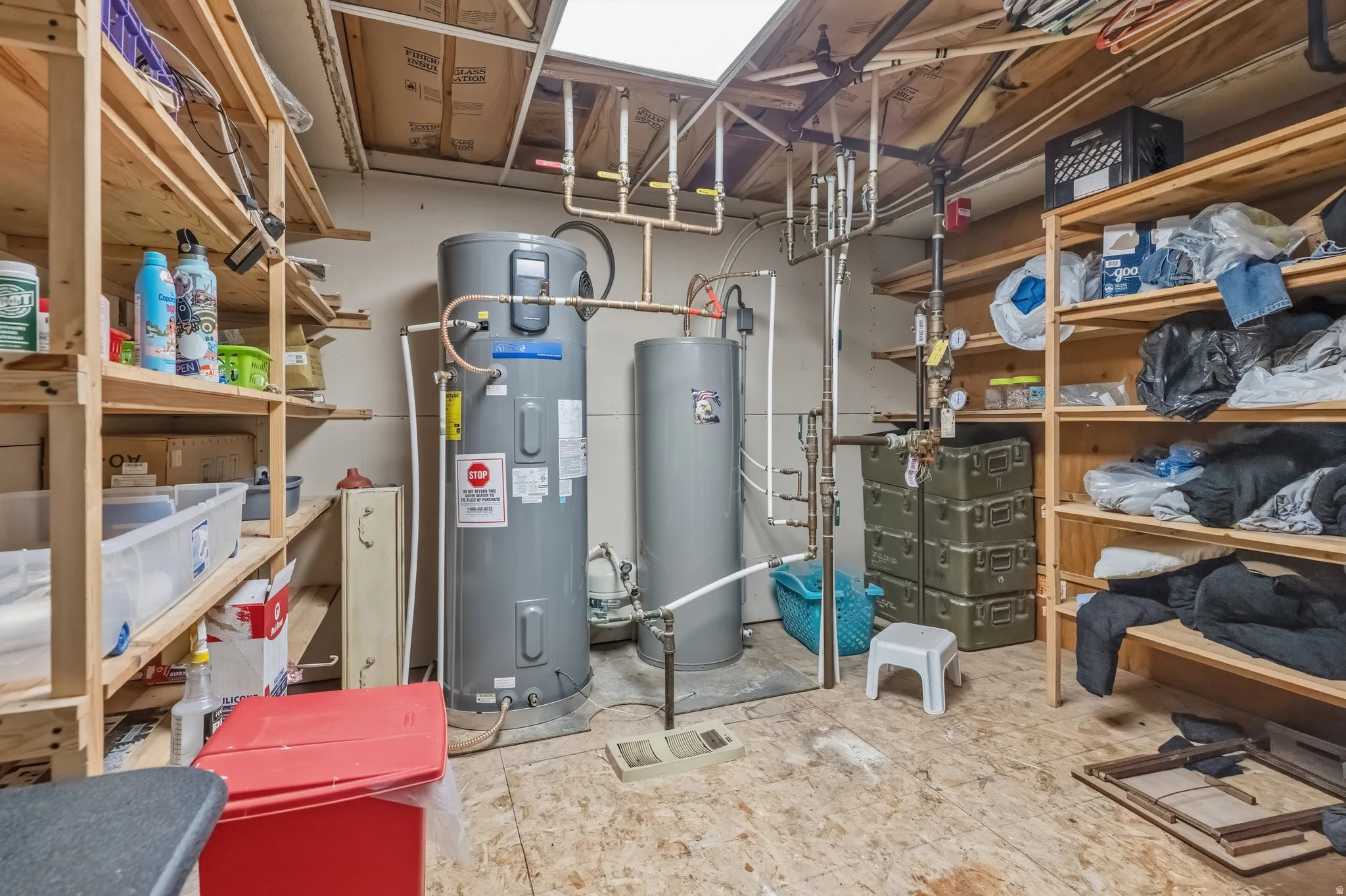 Utility room featuring two water heaters, exposed ceiling joists, and extensive built-in shelving