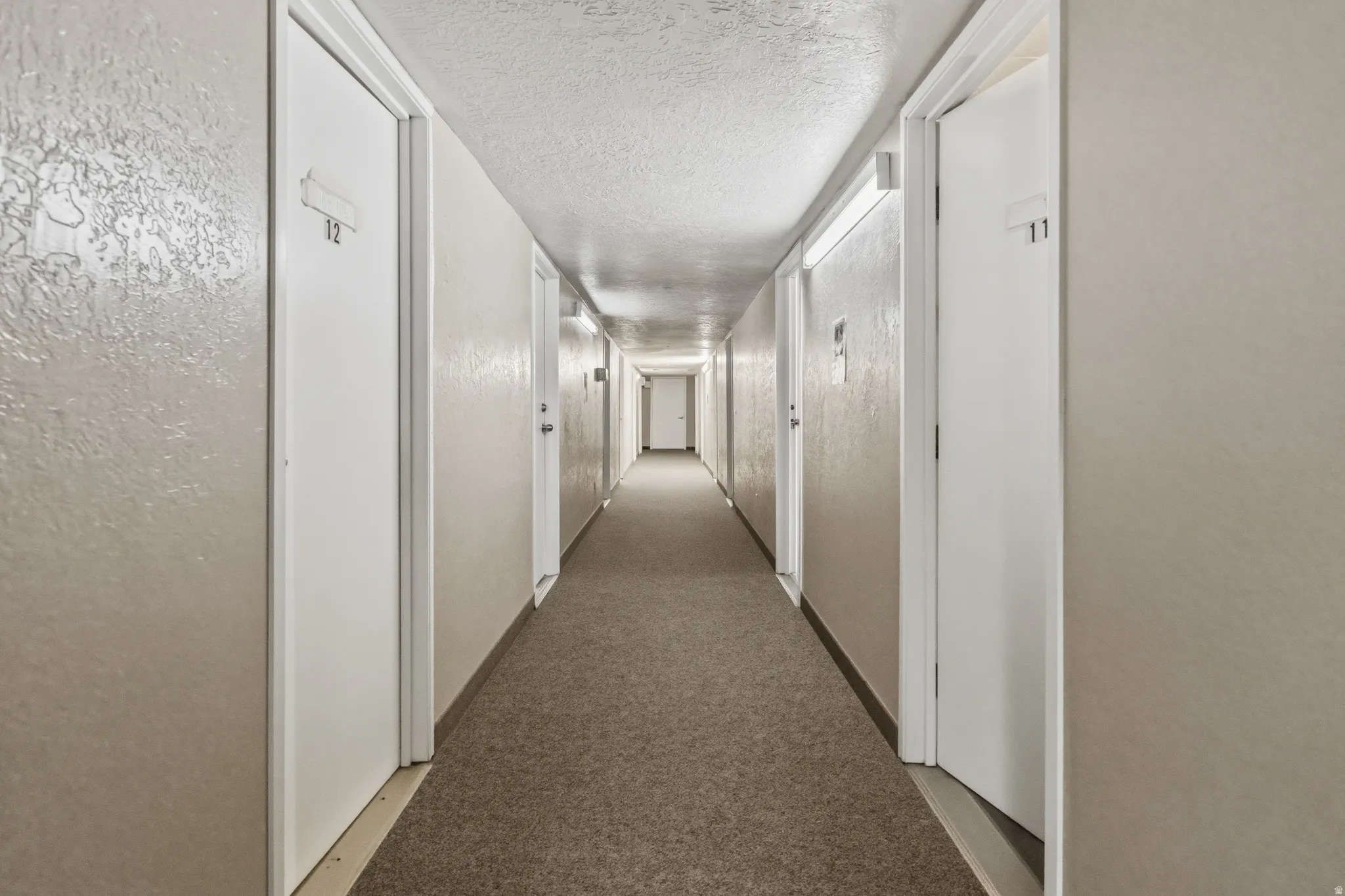Long interior corridor featuring neutral wall finishes and a textured ceiling