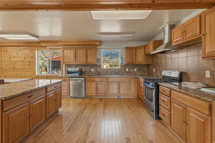Spacious kitchen featuring wood-finish flooring, light wood cabinetry, stone countertops, and stainless steel appliances