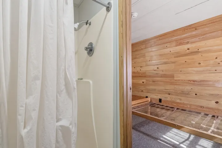 Shower featuring a chrome shower head and controls, a beige surround, and a white shower curtain