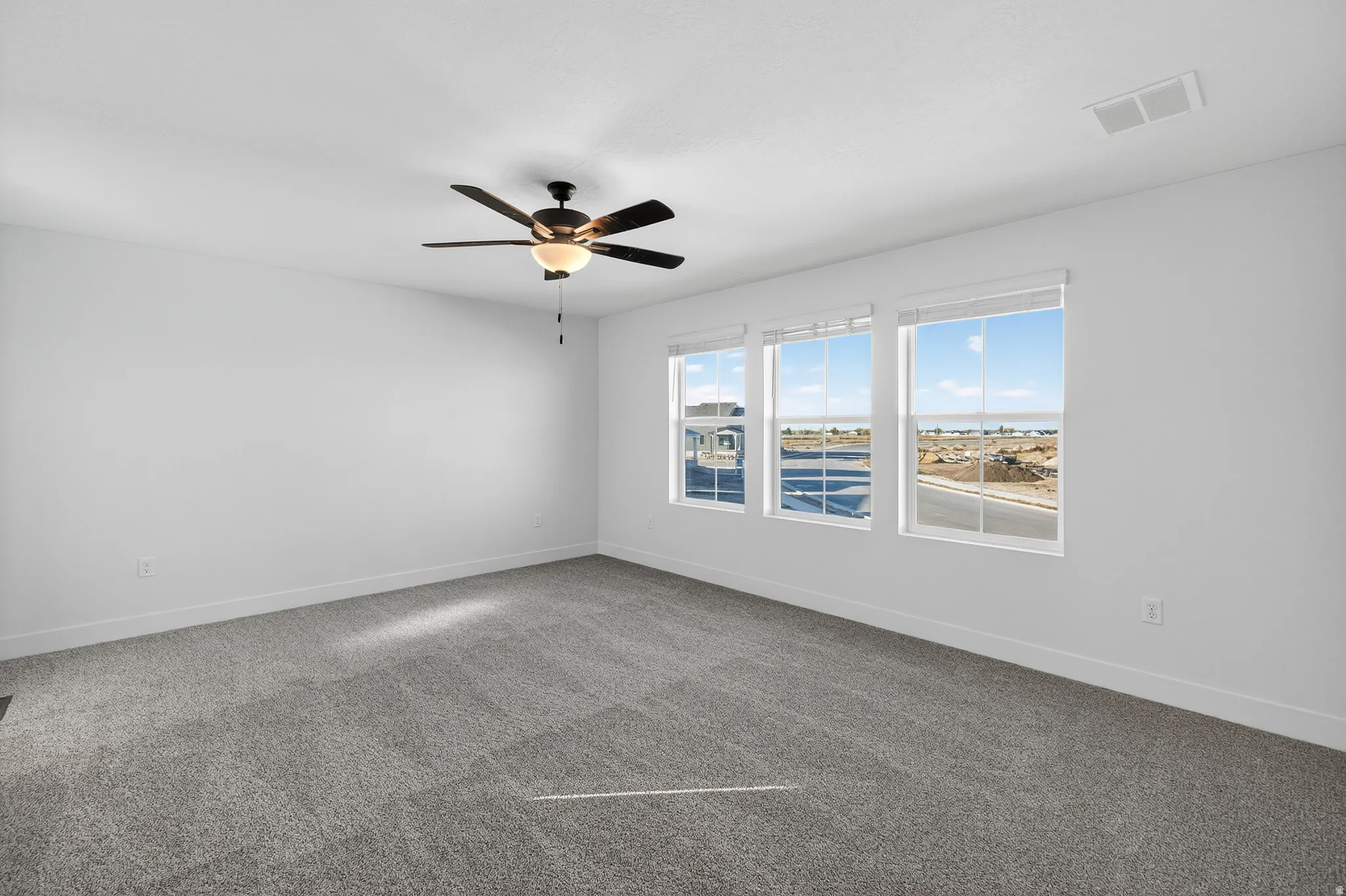 Spacious room featuring three windows, a ceiling fan with integrated lighting, and neutral-toned carpeting