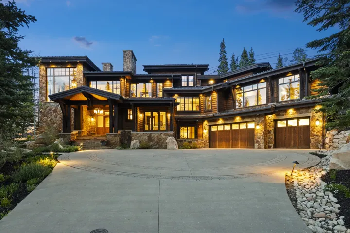 Stone and wood-clad exterior with multiple large windows, a covered entry, and a multi-car garage