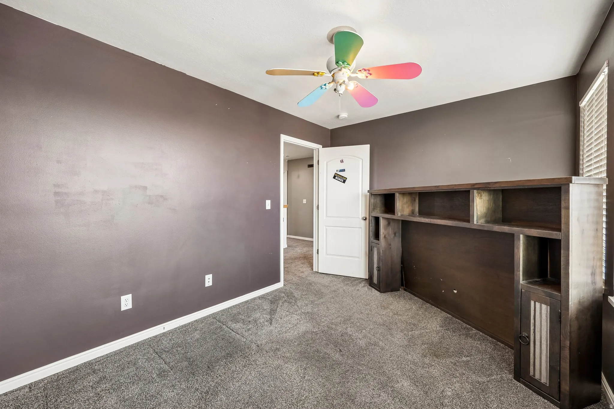 Carpeted room with dark gray walls and a ceiling fan with colorful blades