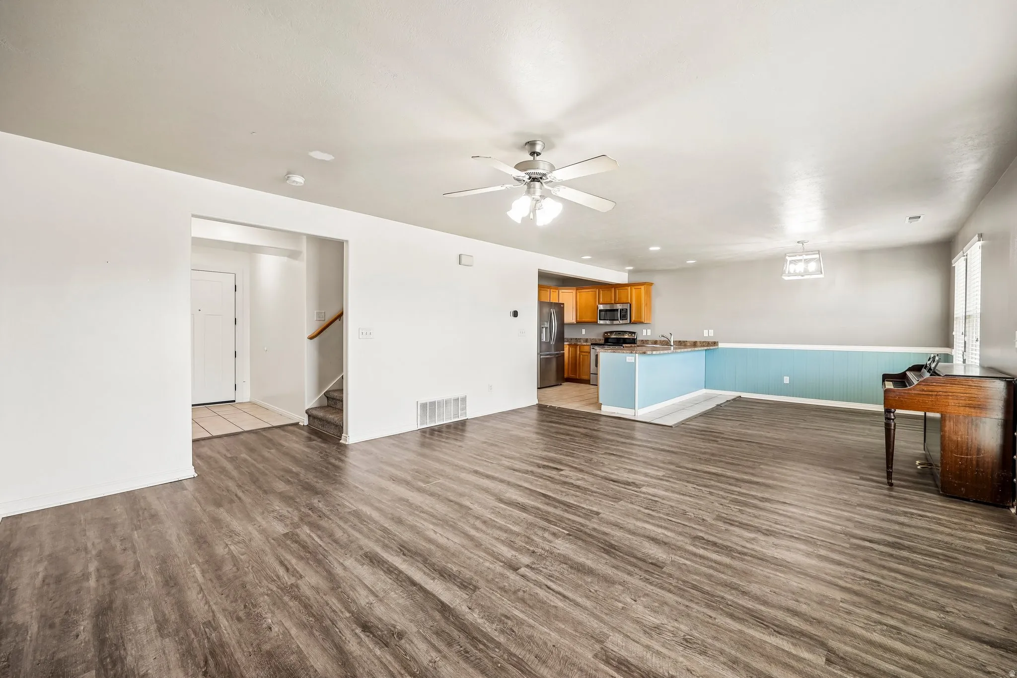 Spacious open-concept living area featuring wood-finish flooring, a ceiling fan with integrated lighting, and neutral wall tones