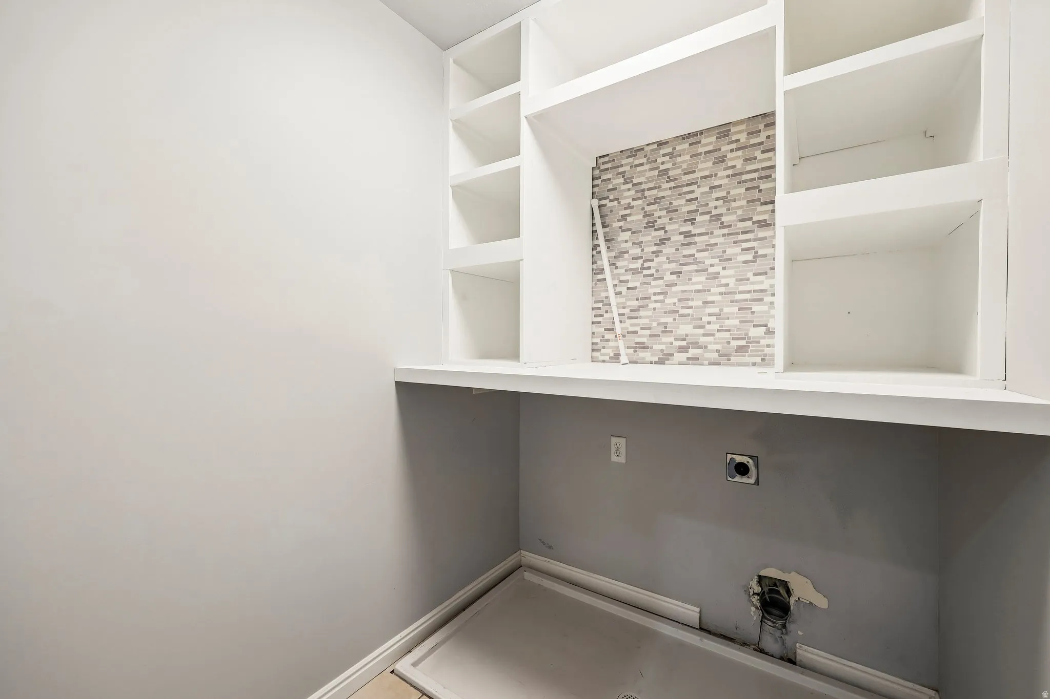 Laundry area featuring a mosaic tile backsplash, built-in shelving, white countertop, and a utility hookup