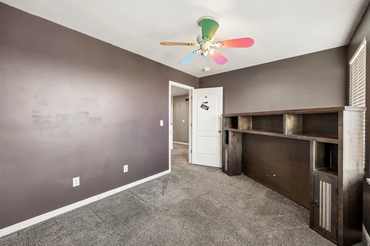 Carpeted room with dark gray walls and a ceiling fan with colorful blades
