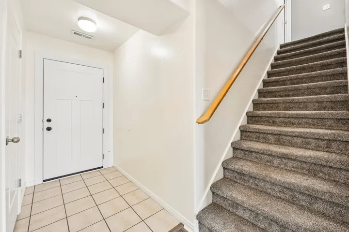 Entryway featuring a white paneled door with dark hardware, square tile flooring, and a carpeted staircase with a wood handrail