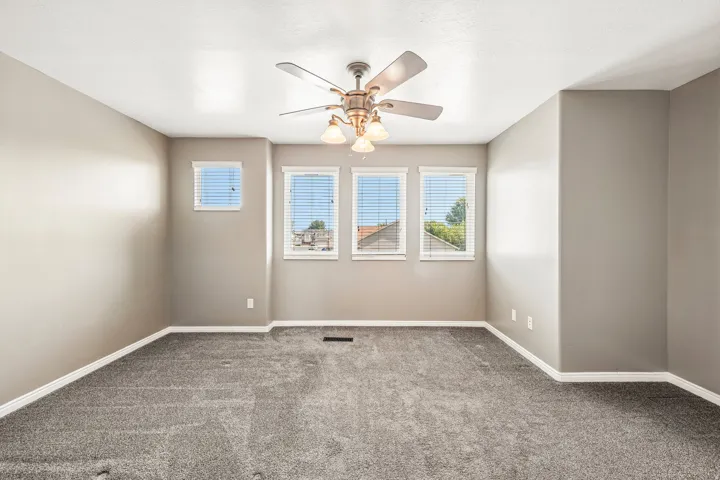 Interior room featuring neutral wall paint, gray carpeting, a ceiling fan with integrated lighting, and multiple windows with horizontal blinds