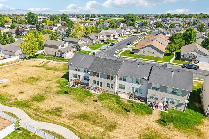 Rear exterior of a multi-story townhome featuring a private deck, ground-level patio, and a grass lawn